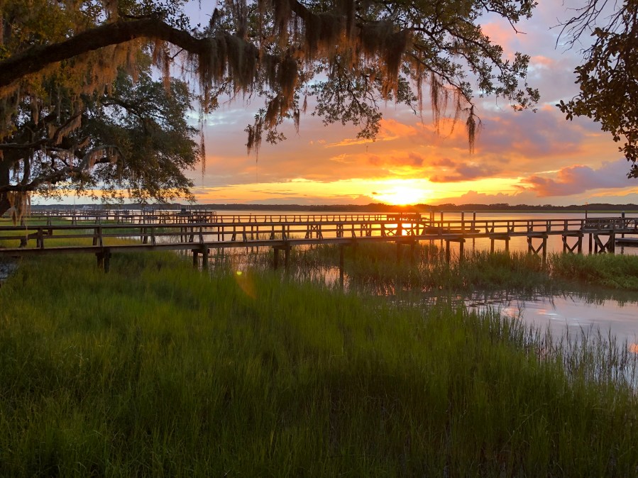 A sunset over the water with a bridge in the foreground.