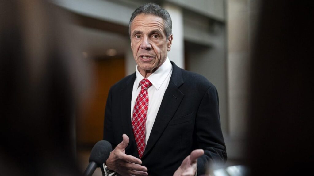 A man in a suit and tie talking into microphones.