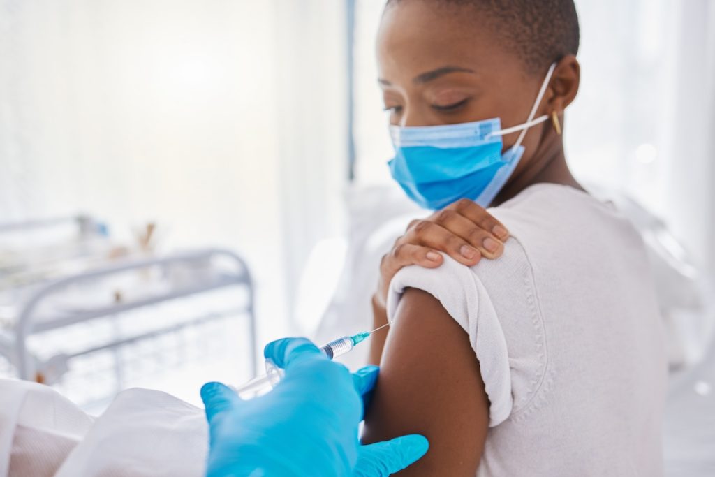 A person with a mask and gloves getting their arm examined.