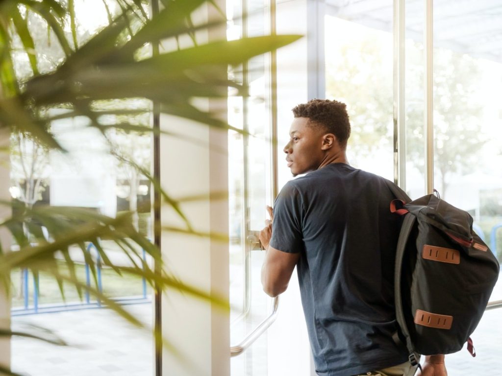 A man with a backpack and headphones standing in front of a window.