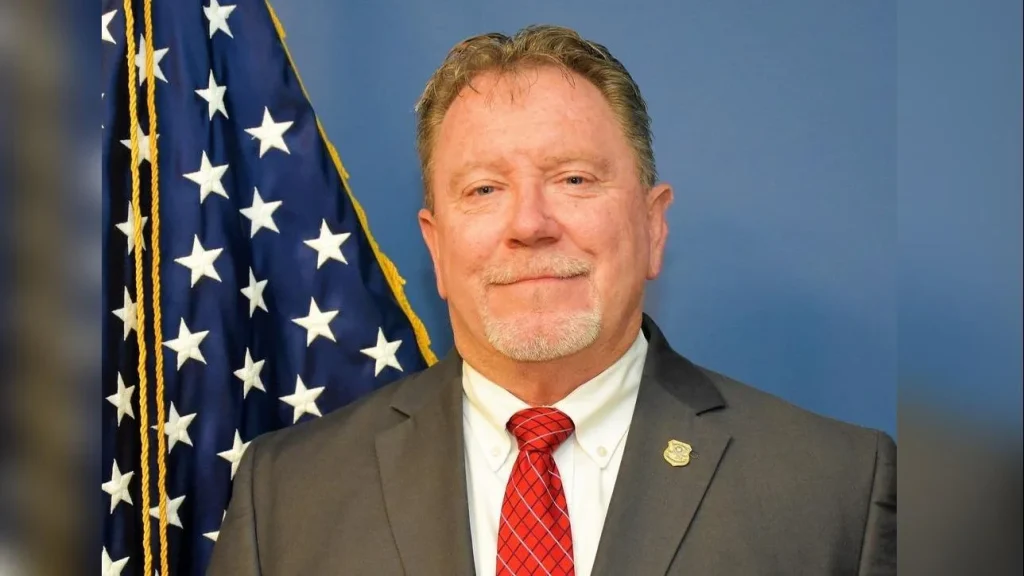 A man in a suit and tie next to an american flag.