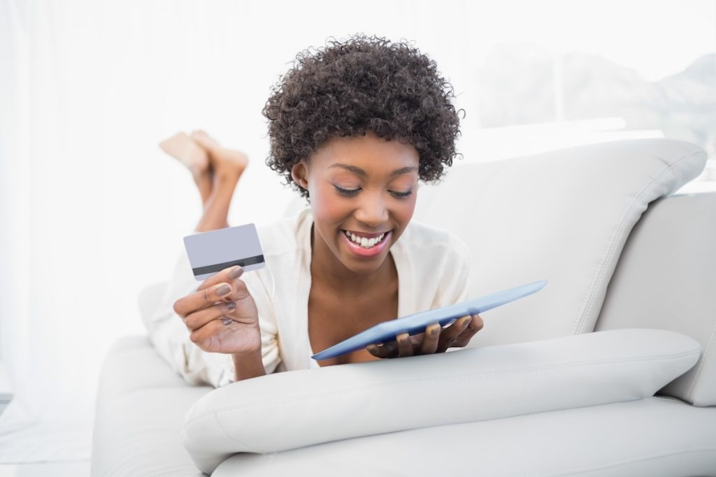 A woman is holding her credit card and looking at the ipad.