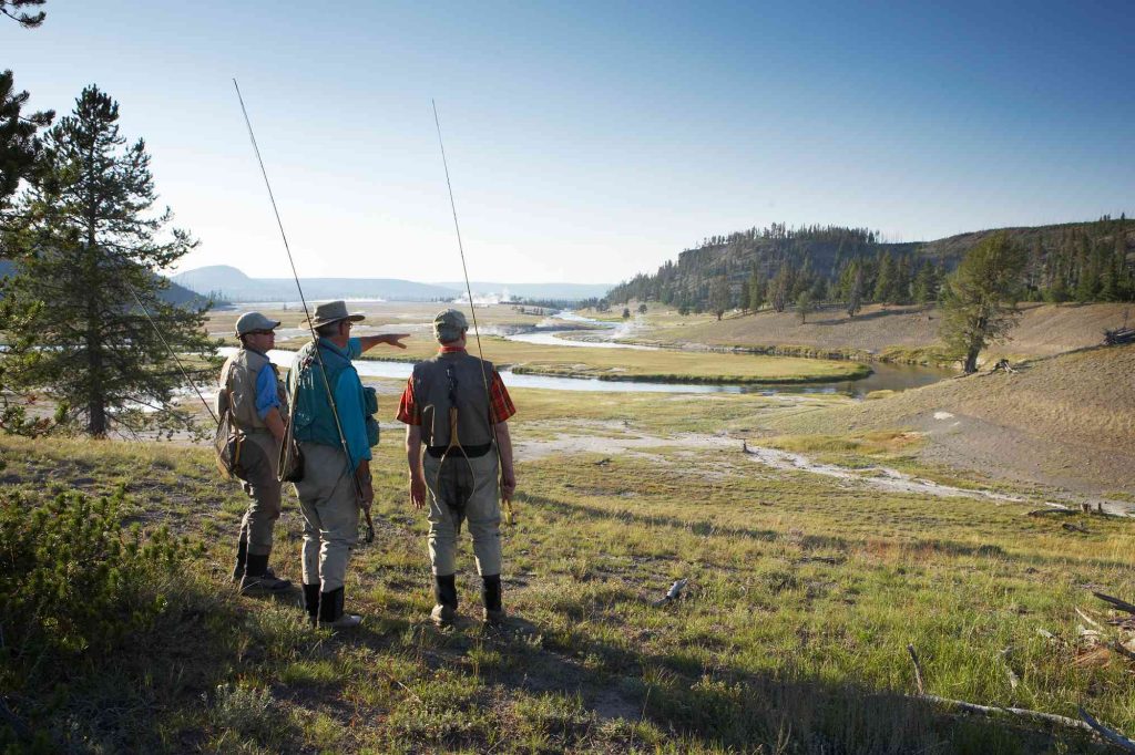 Three men standing on a hill with fishing rods.