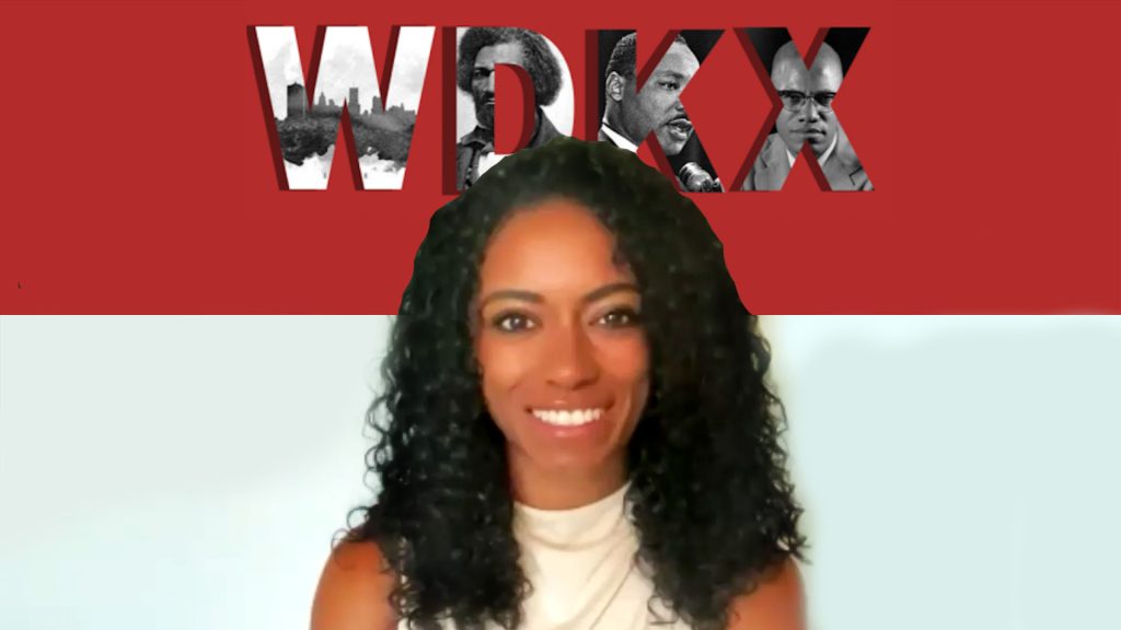 A woman with long black hair and white shirt in front of red letters.