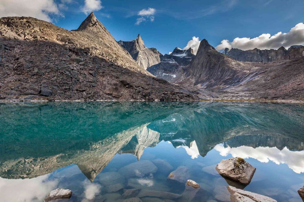 A mountain range with water and rocks in the foreground.