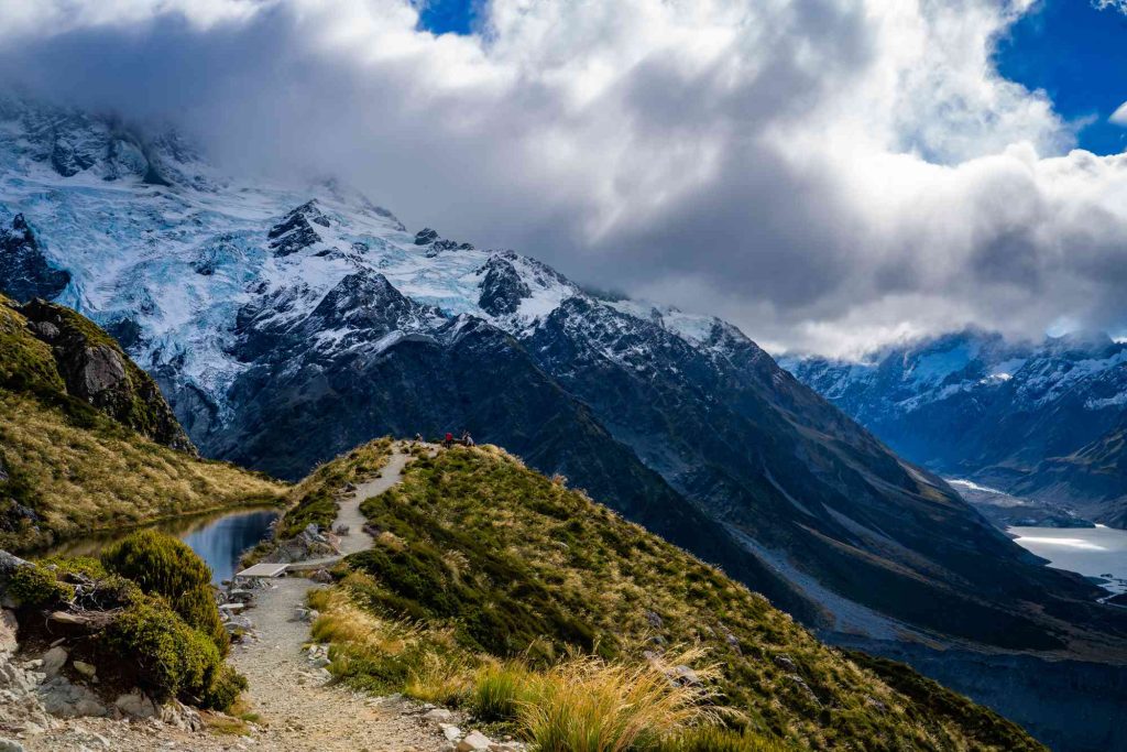 A trail on the side of a mountain with snow capped mountains in the background.