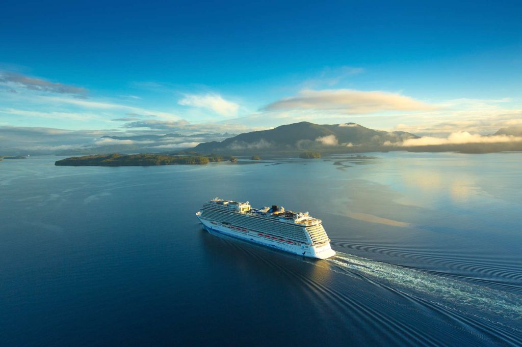 A cruise ship sailing on the ocean with mountains in the background.