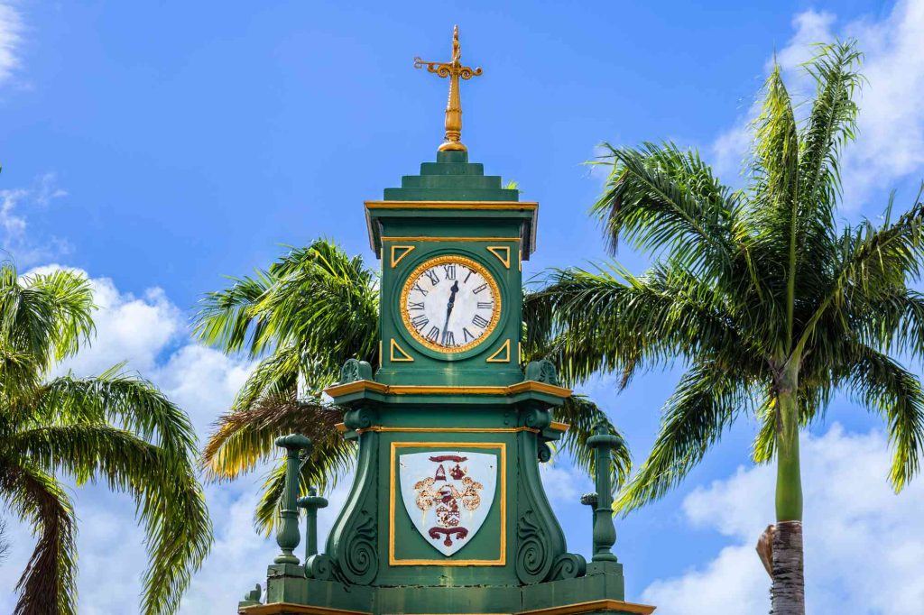 A green clock tower with a cross on top of it.