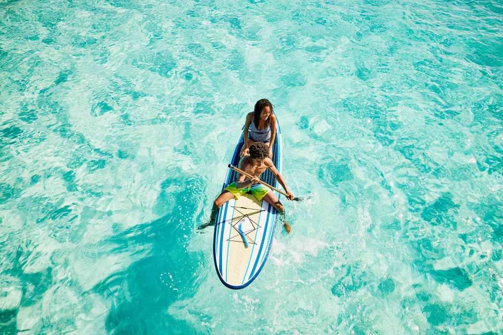 A woman and child are on a surfboard in the water.