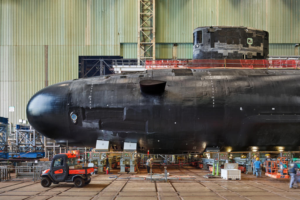 A black submarine in an industrial setting with workers.