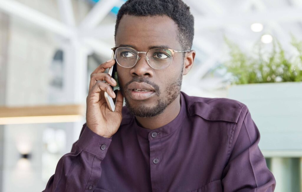 A man in purple shirt holding a cell phone to his ear.