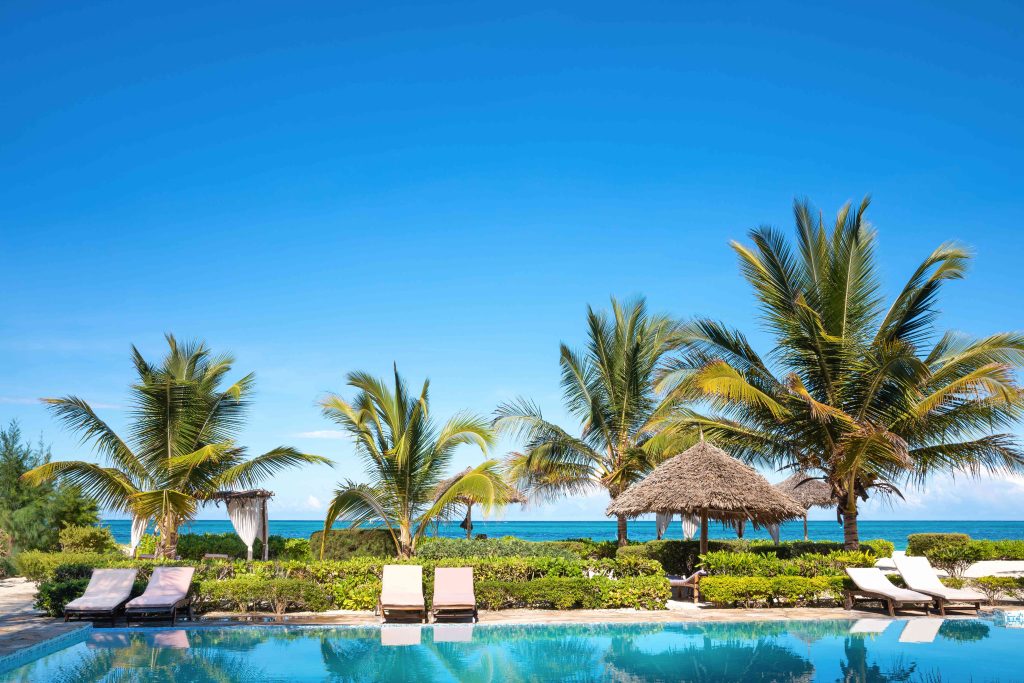 A pool with chairs and umbrellas next to the ocean.