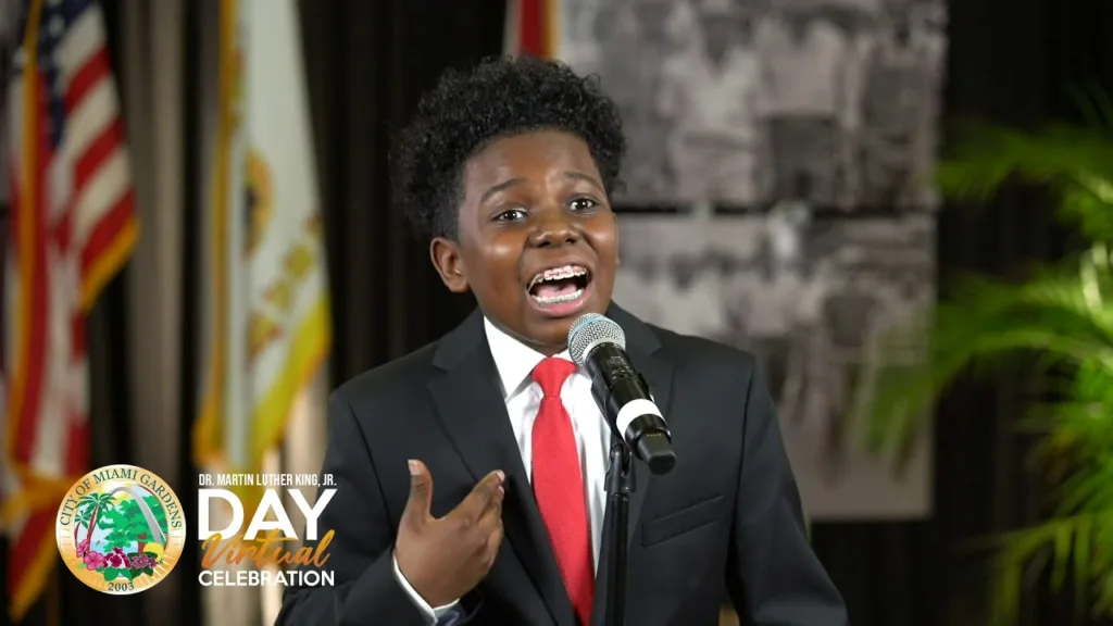 A young boy in suit and tie speaking into microphone.