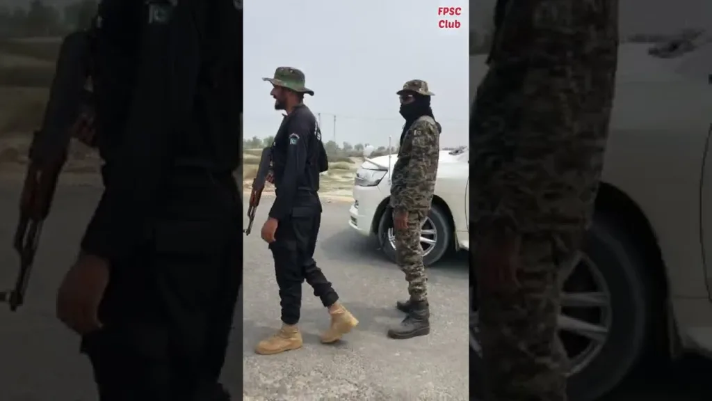 Two men in camouflage outfits stand on a street.