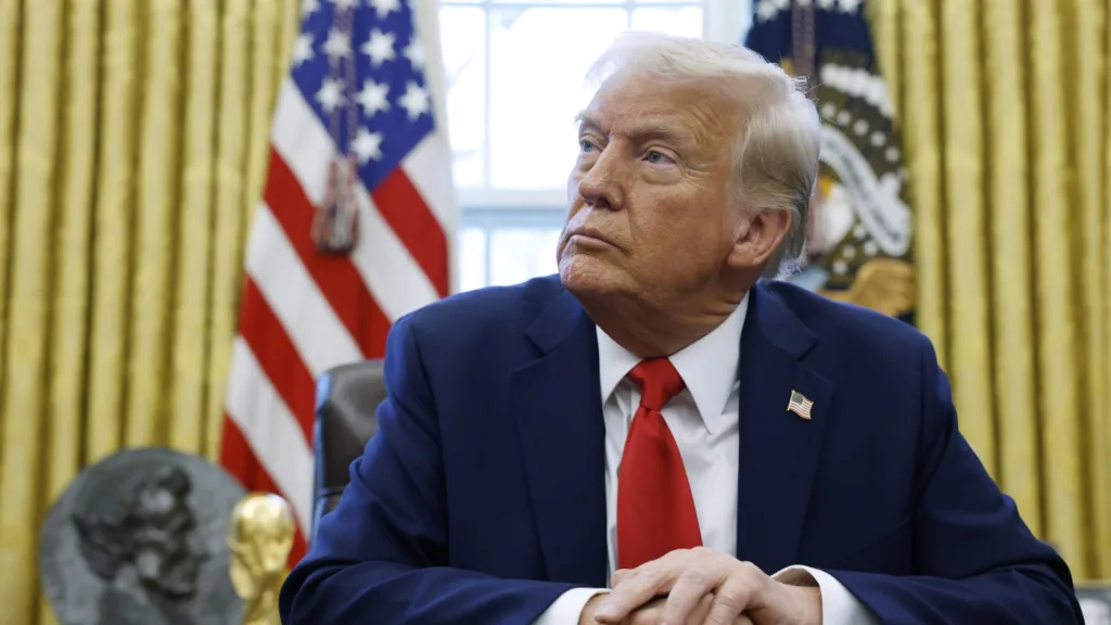 Trump government actions on schools, colleges : NPR Man sitting in office with flags behind.