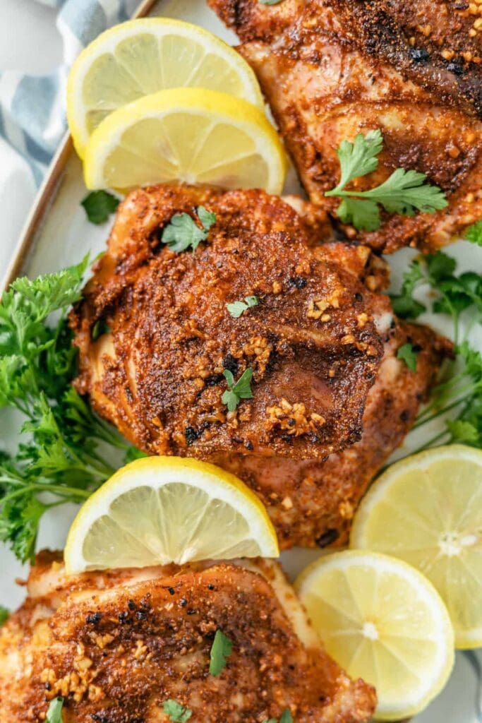 Plateful of crispy baked bone-in chicken thighs artfully arranged with vibrant parsley and lemon slices