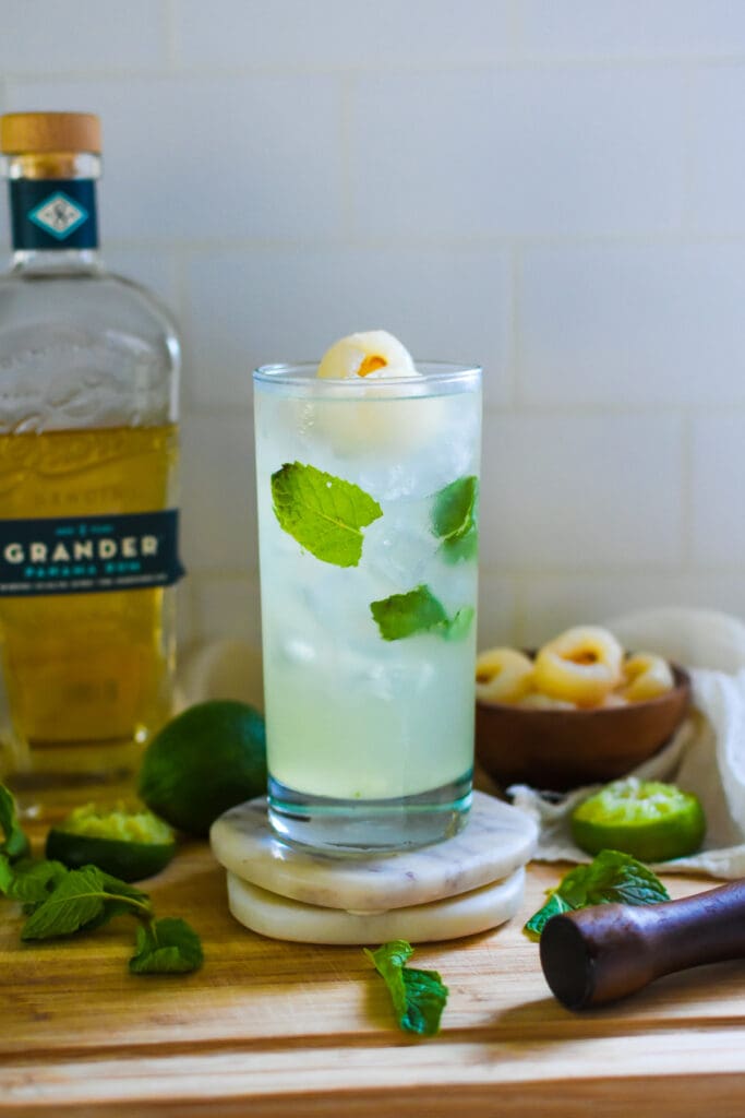 homemade, easy lychee mojito cocktail served in a highball glass with floating mint leaves and lychee fruit.