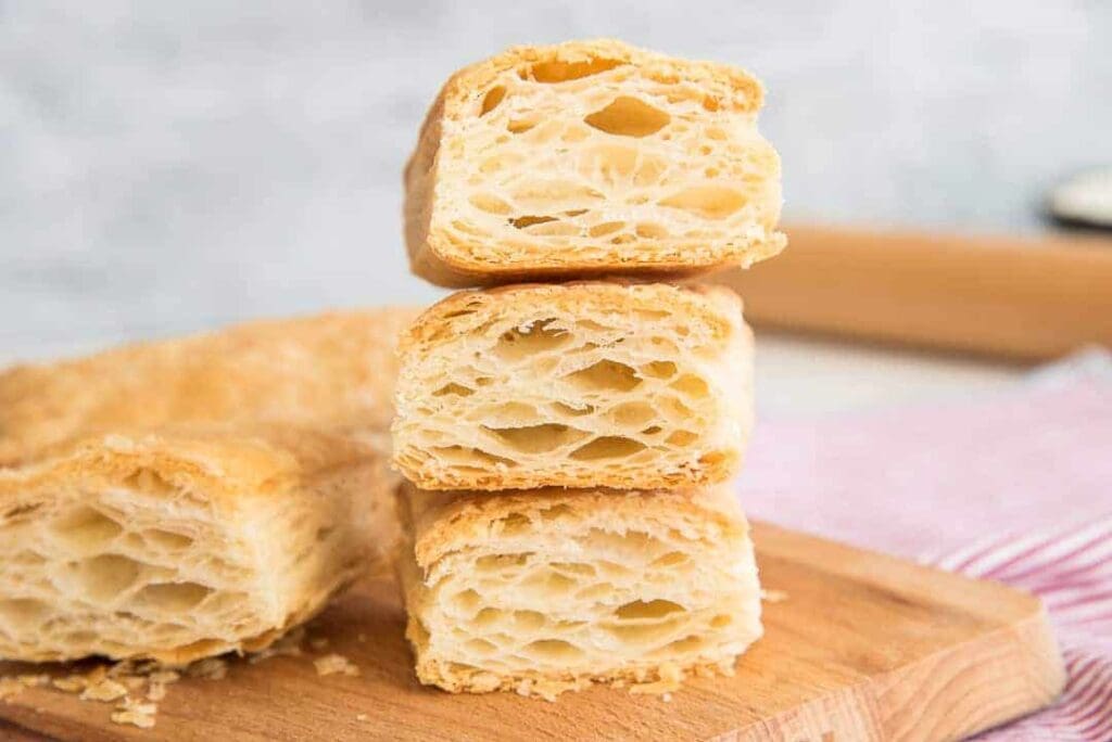 Flaky puff pastry pieces on wooden board.
