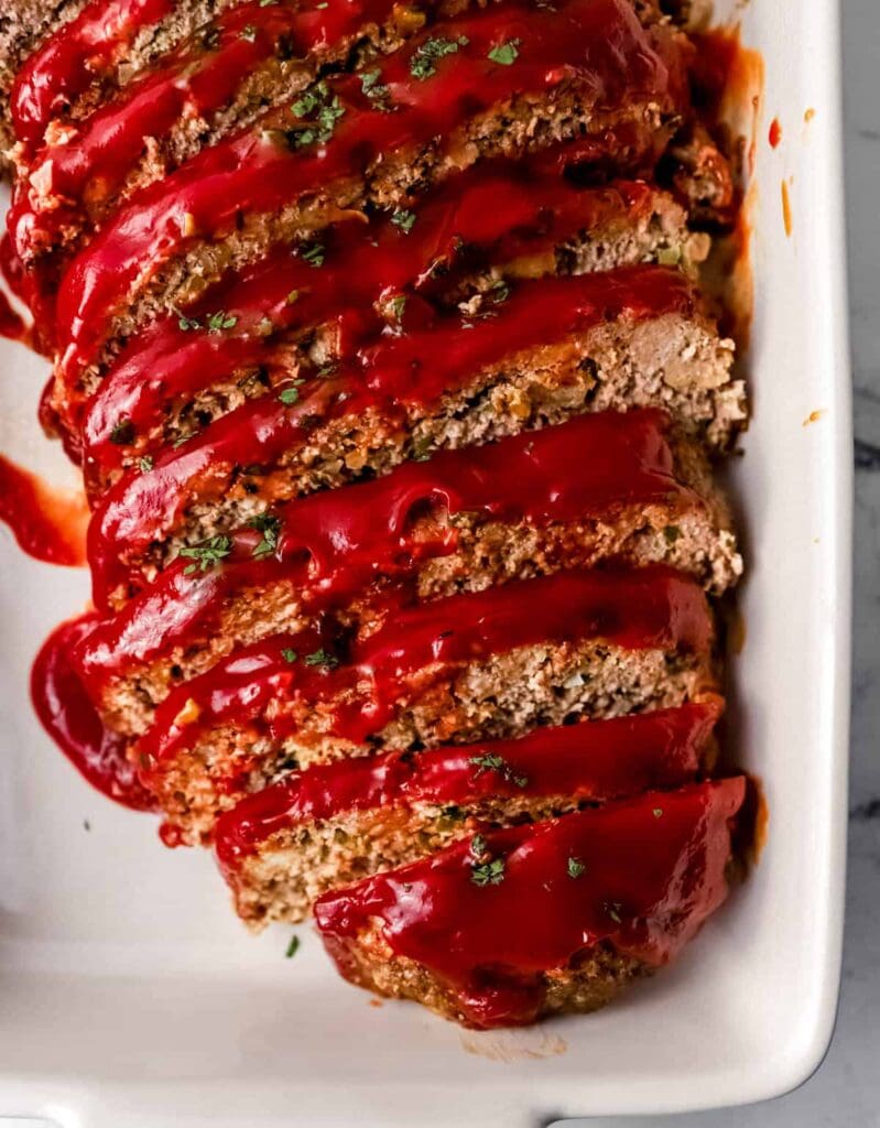 Overhead view of sliced meatloaf topped with sauce in white baking dish.
