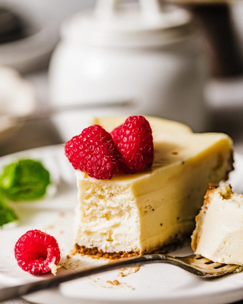 a slice of mascarpone cheesecake on a plate with fresh raspberries and mint.