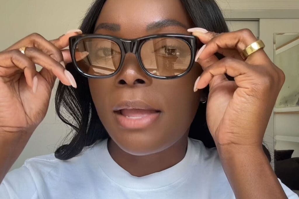 Woman adjusting large black glasses indoors.