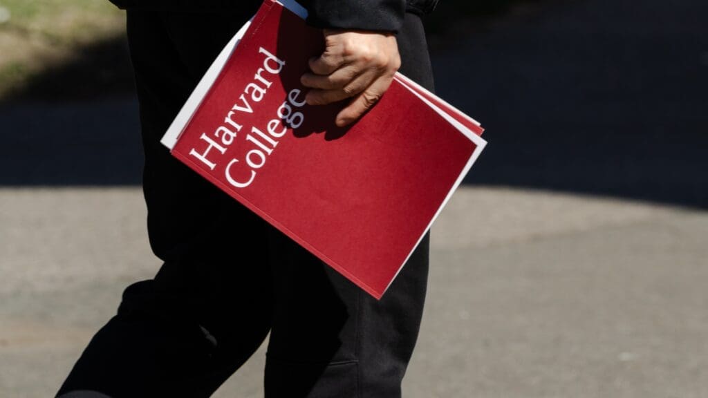 Person holding Harvard College folder outdoors.