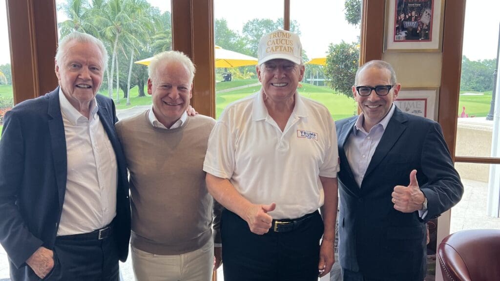 Four men standing indoors, smiling together.