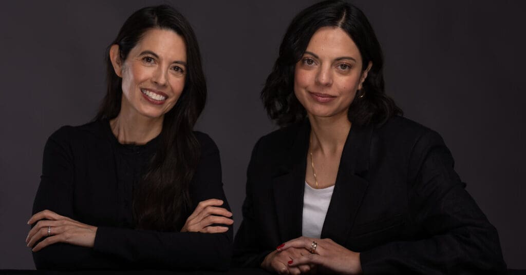 Two women smiling in a dark setting.