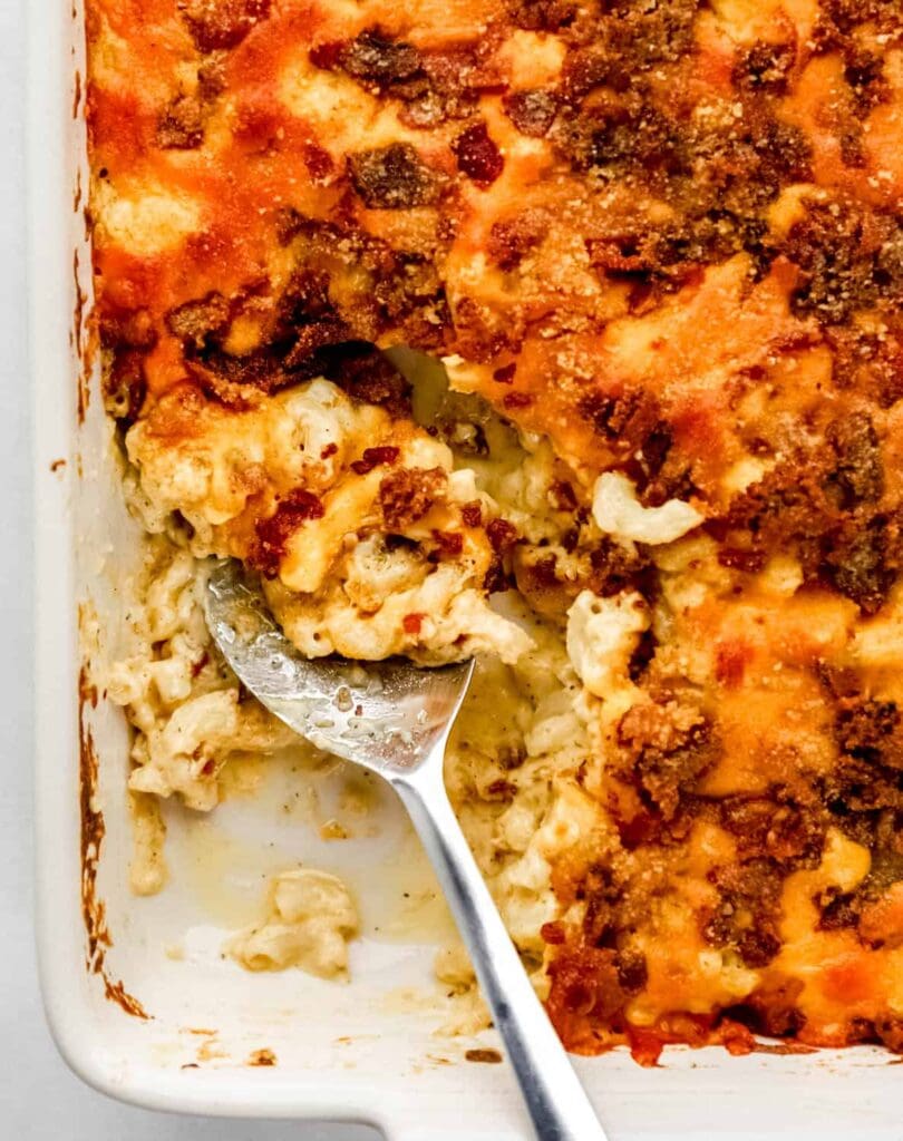 Overhead view of bacon mac and cheese in white bacon dish with serving spoon in it.