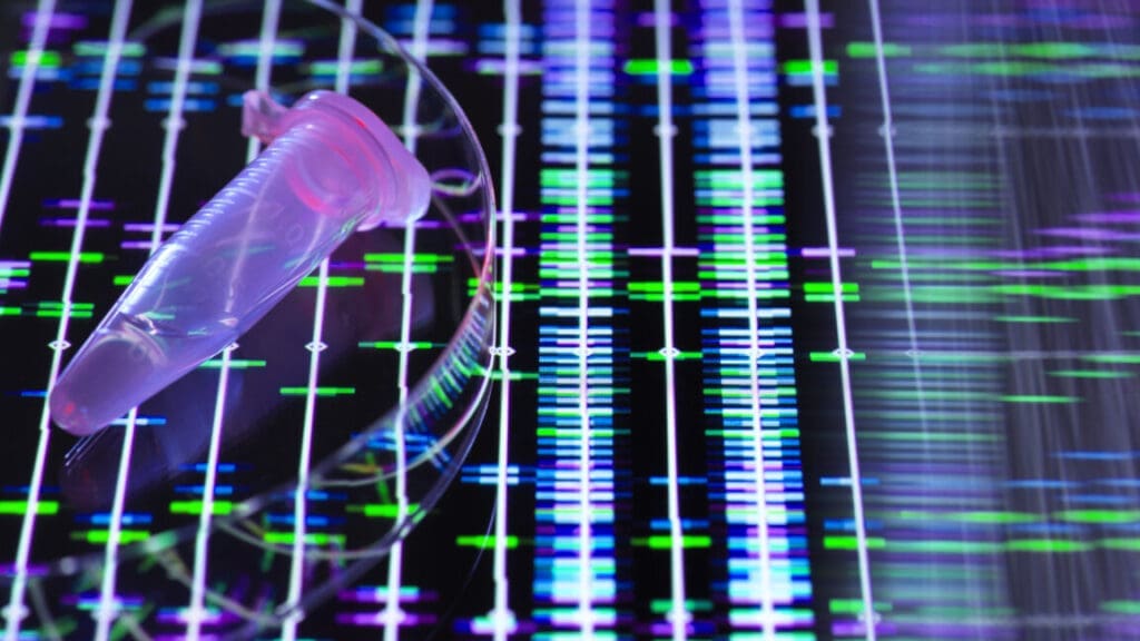 Image of a small sample tube in front of a screen covered in fluorescent bands that represent DNA sequences.