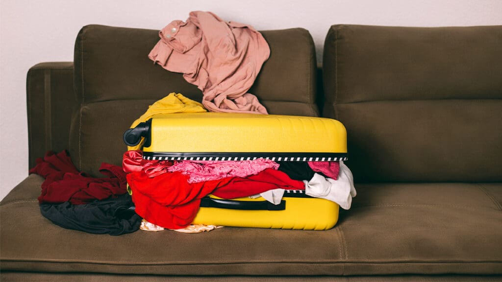 Clothes spilling from yellow suitcase on couch.
