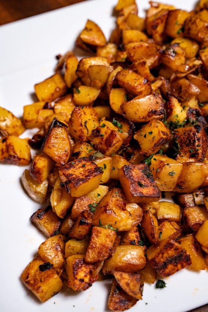 Frying Pan Morning Meal Potatoes – Cage Can Prepare Roasted diced potatoes on a white plate.
