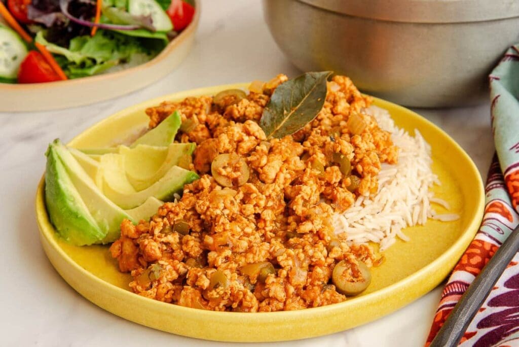 A closeup shot of the turkey picadillo on a bed of white rice on a yellow plate.