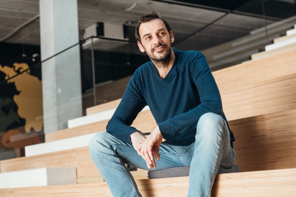Man sitting on wooden steps, smiling casually.