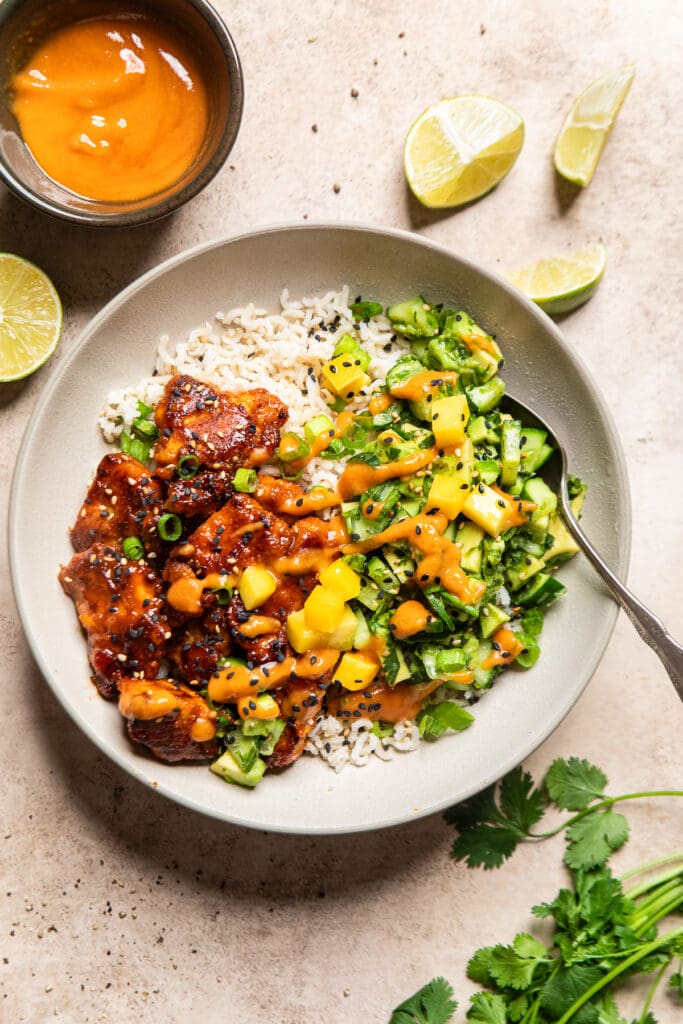 a bowl filled with rice, spicy maple tofu, and a cucumber avocado salad.