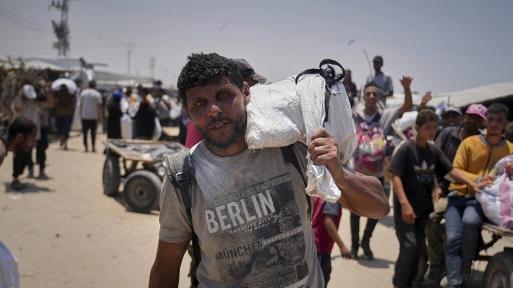 Man carrying belongings in crowded outdoor setting.
