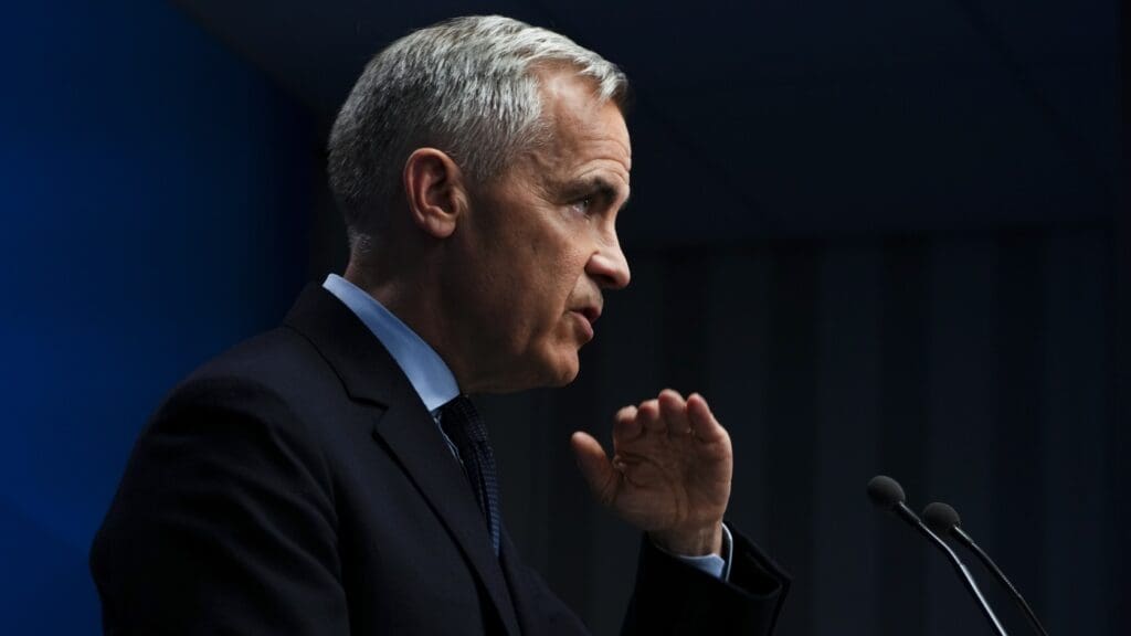 Man speaking at a podium, dark background.