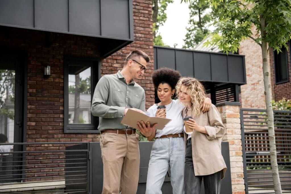An interracial lesbian couple looking over a home inspection report and other paperwork with their realtor in front of their potential future home