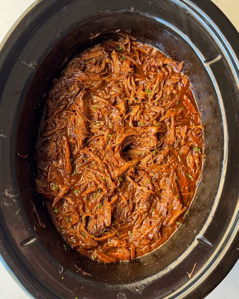 overhead shot of cooked, shredded BBQ Beef in a black slow cooker