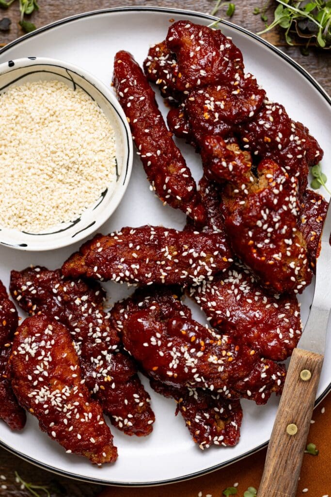 Delicious Gochujang Chicken Tenders on a white platter with a side of sesame seeds and a fork.