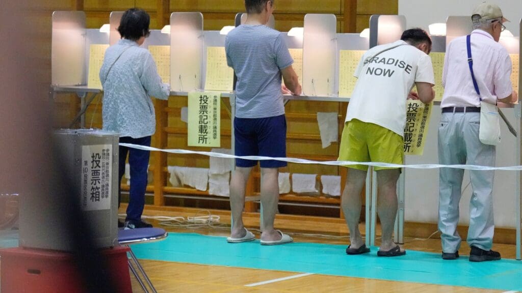 People voting at polling booths in gymnasium.