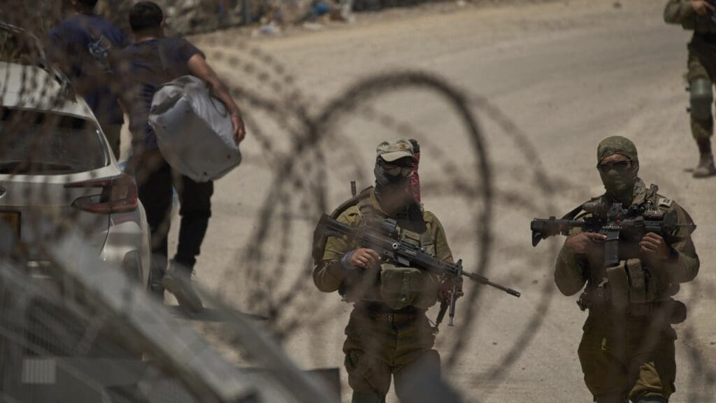 Soldiers with weapons behind barbed wire fence.