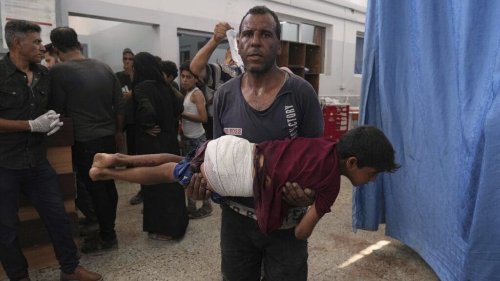 Man carrying injured child in crowded room.