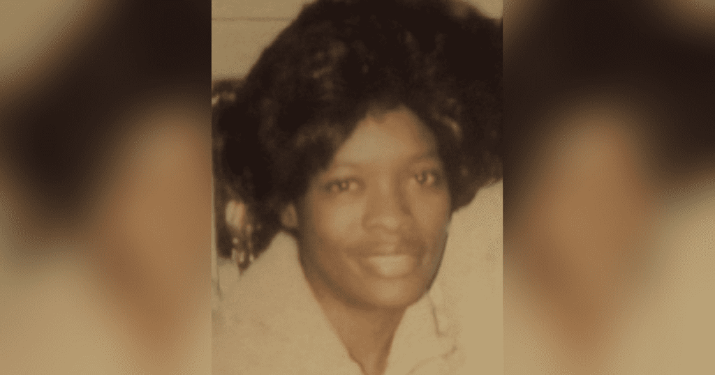 Smiling person with dark hair and coat.