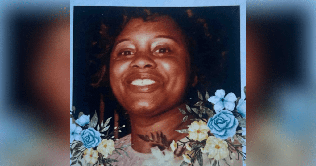 Smiling woman surrounded by blue and yellow flowers.