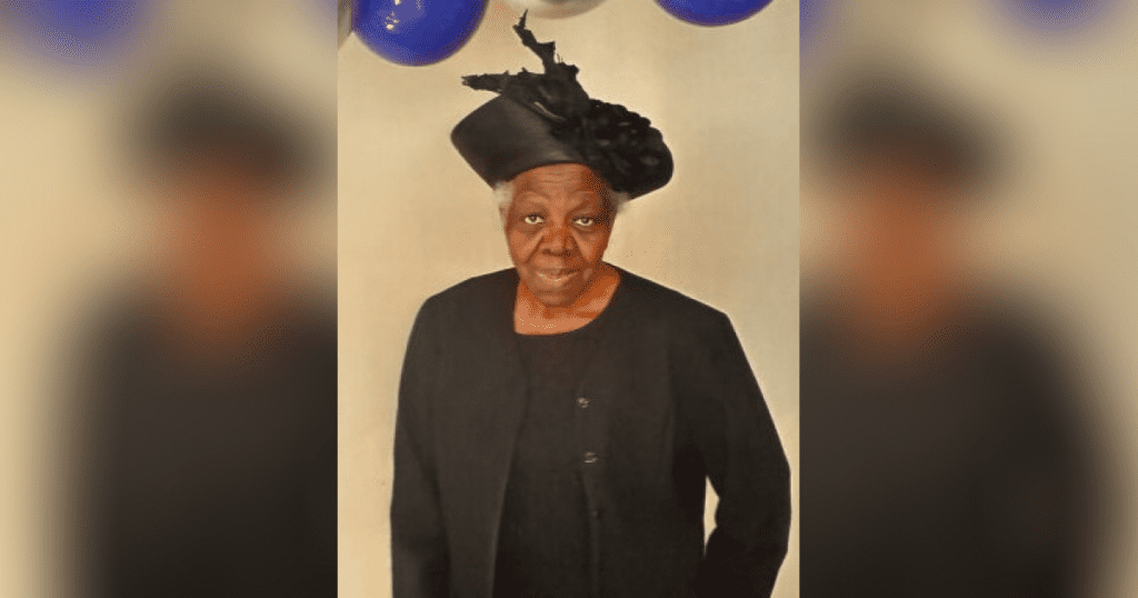 Elderly woman in black outfit and hat.