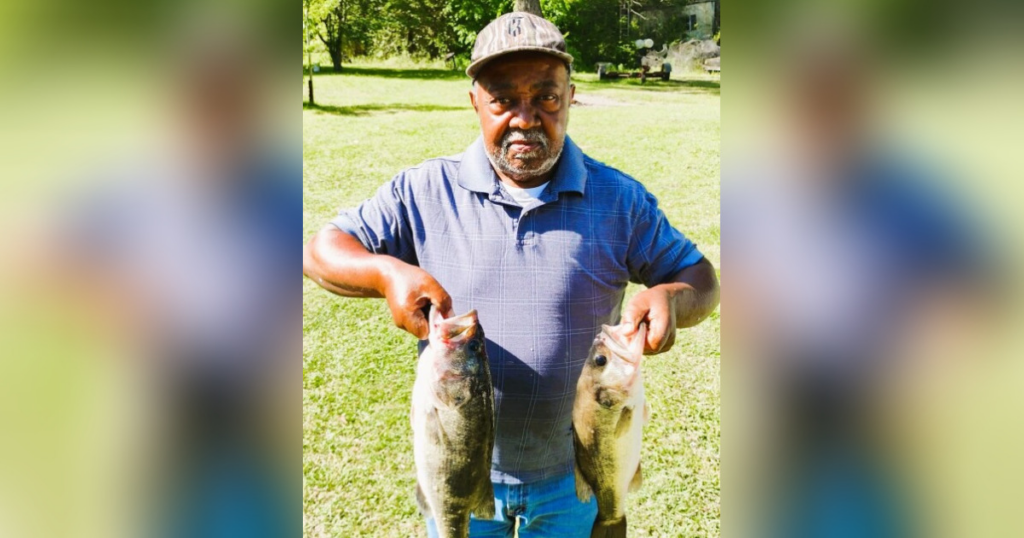 Man holding two large fish outdoors.