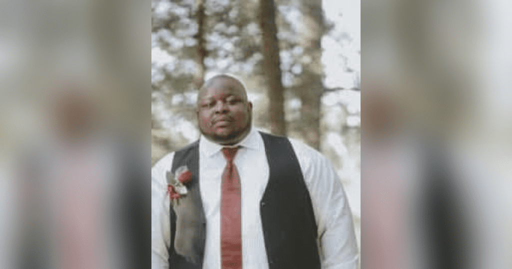 Man in formal attire outdoors with trees.