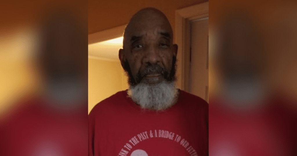 Man in red shirt, standing indoors.
