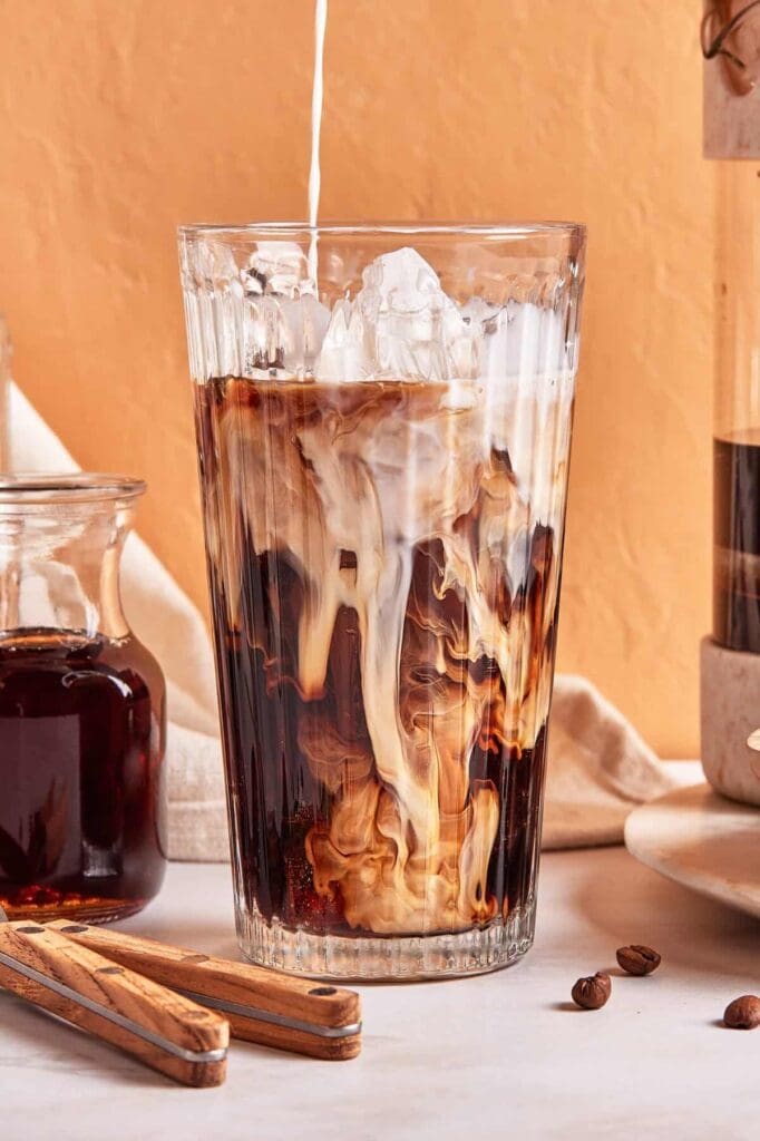 Iced coffee with milk pouring in.